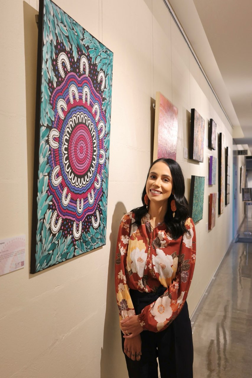 Photo of Stephanie Singh-Highfold next to one of her pieces of art.